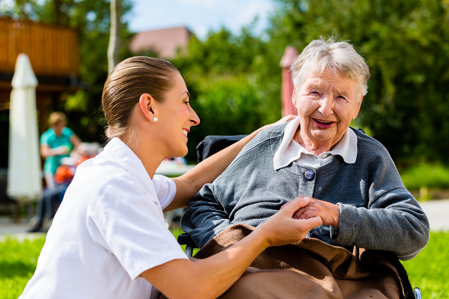 Nurse holding hands with senior woman sitting in wheelchair in garden of retirement home